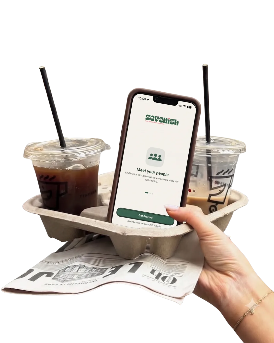 A hand holding a fiber coffee-carrier tray with two iced coffees and a phone showing the Sevenish app's 'Meet your people' welcome screen